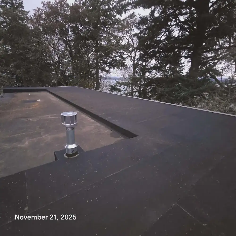 Flat roof with a vent, trees behind it under a cloudy sky. November 21, 2025.